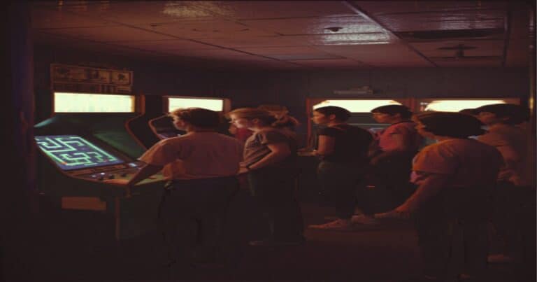 Teenagers in 1980s fashion gathered around arcade game machines in a glowing arcade hall