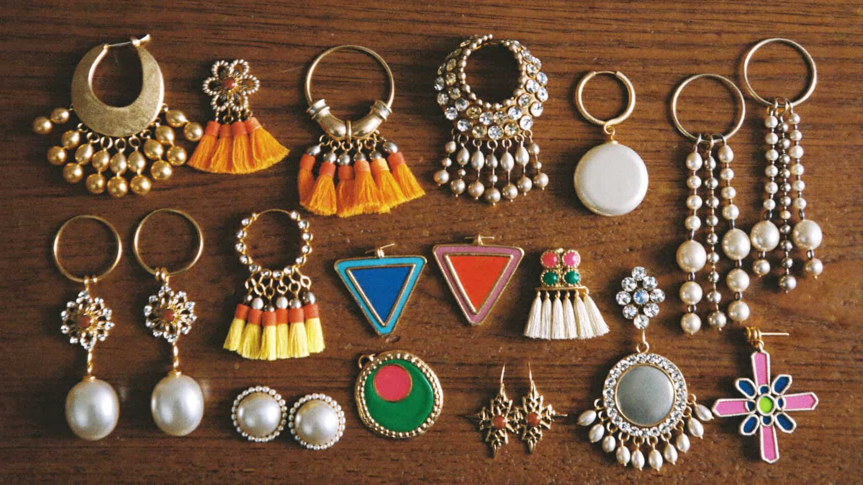 Flat lay of 1980s statement earrings including gold door-knocker hoops, neon geometric shapes, tassel chandeliers and oversized button clip-ons