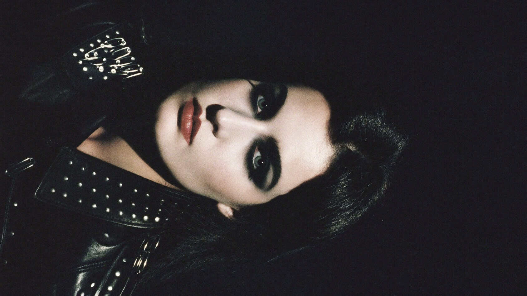 1980s punk woman with deep black-cherry plum lipstick, pale skin, heavy kohl eyeliner and studded leather collar