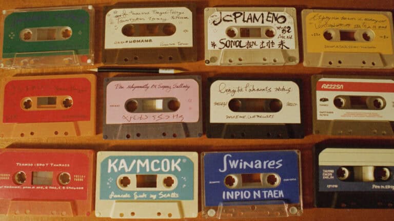 Flat-lay of 1980s mixtape cassette tapes with handwritten J-card inserts on wood surface