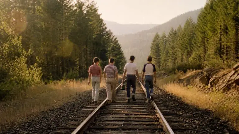 Four boys walking along railroad tracks through a Pacific Northwest forest in golden summer light