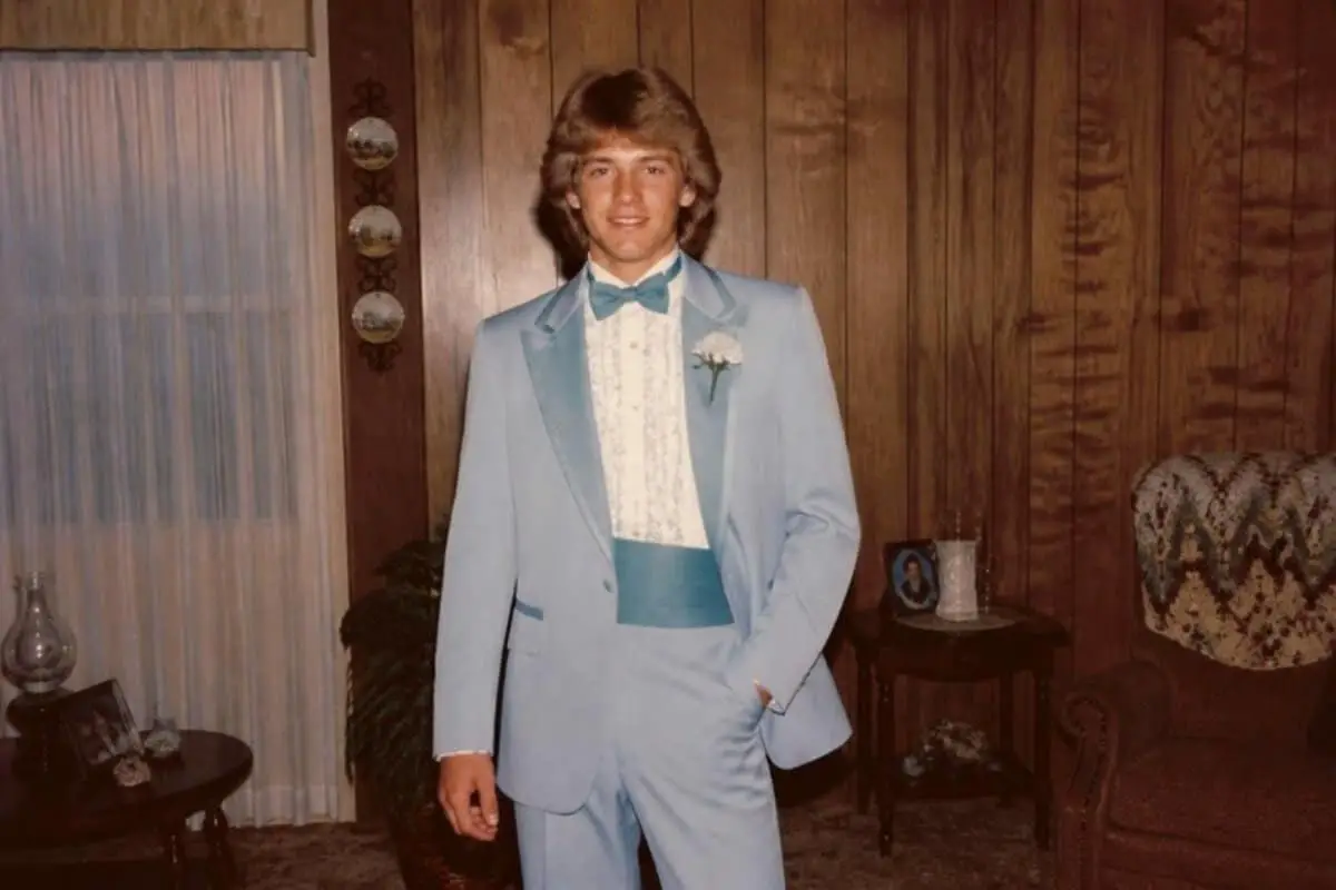 Young man in a powder blue 80s prom tux with ruffled shirt, teal bow tie and matching teal cummerbund