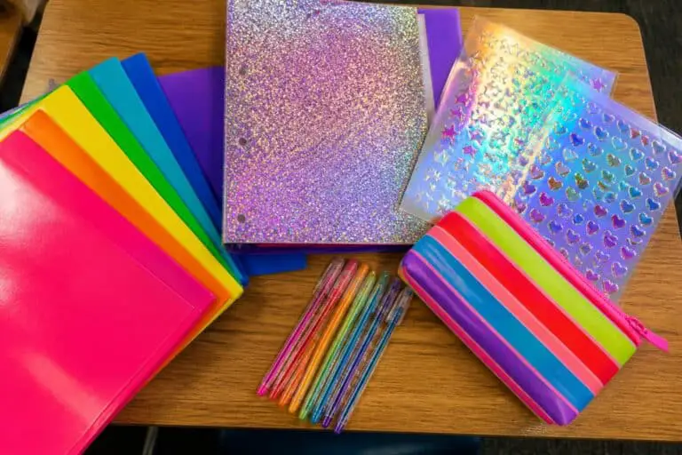Overhead view of a 90s school desk with rainbow folders, a glitter binder, gel pens and holographic stickers