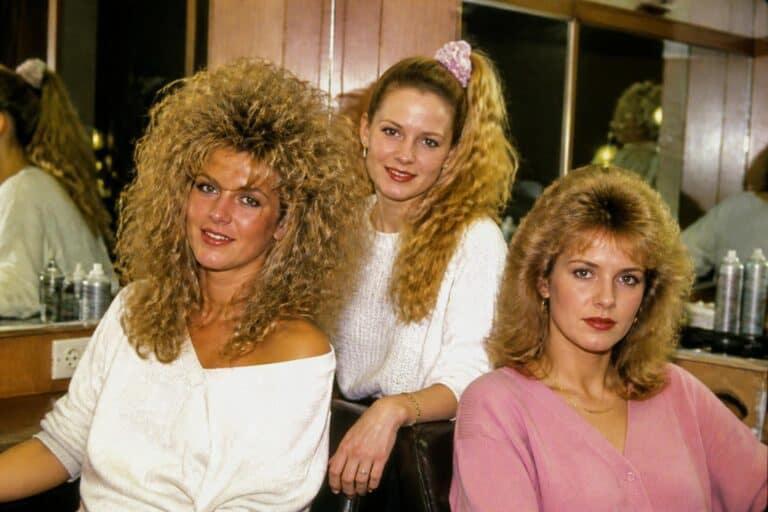 Three women in an 80s salon showing off big teased perms and feathered hairstyles