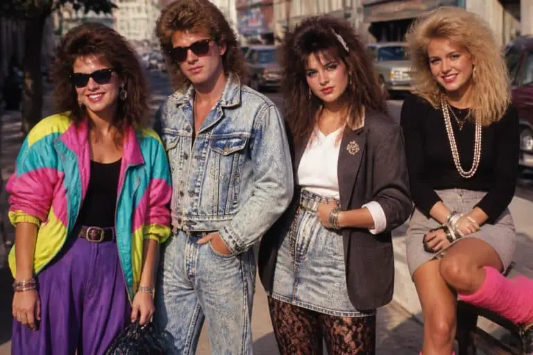 Four friends posing on a city street in neon windbreakers, acid wash denim and big 80s hair
