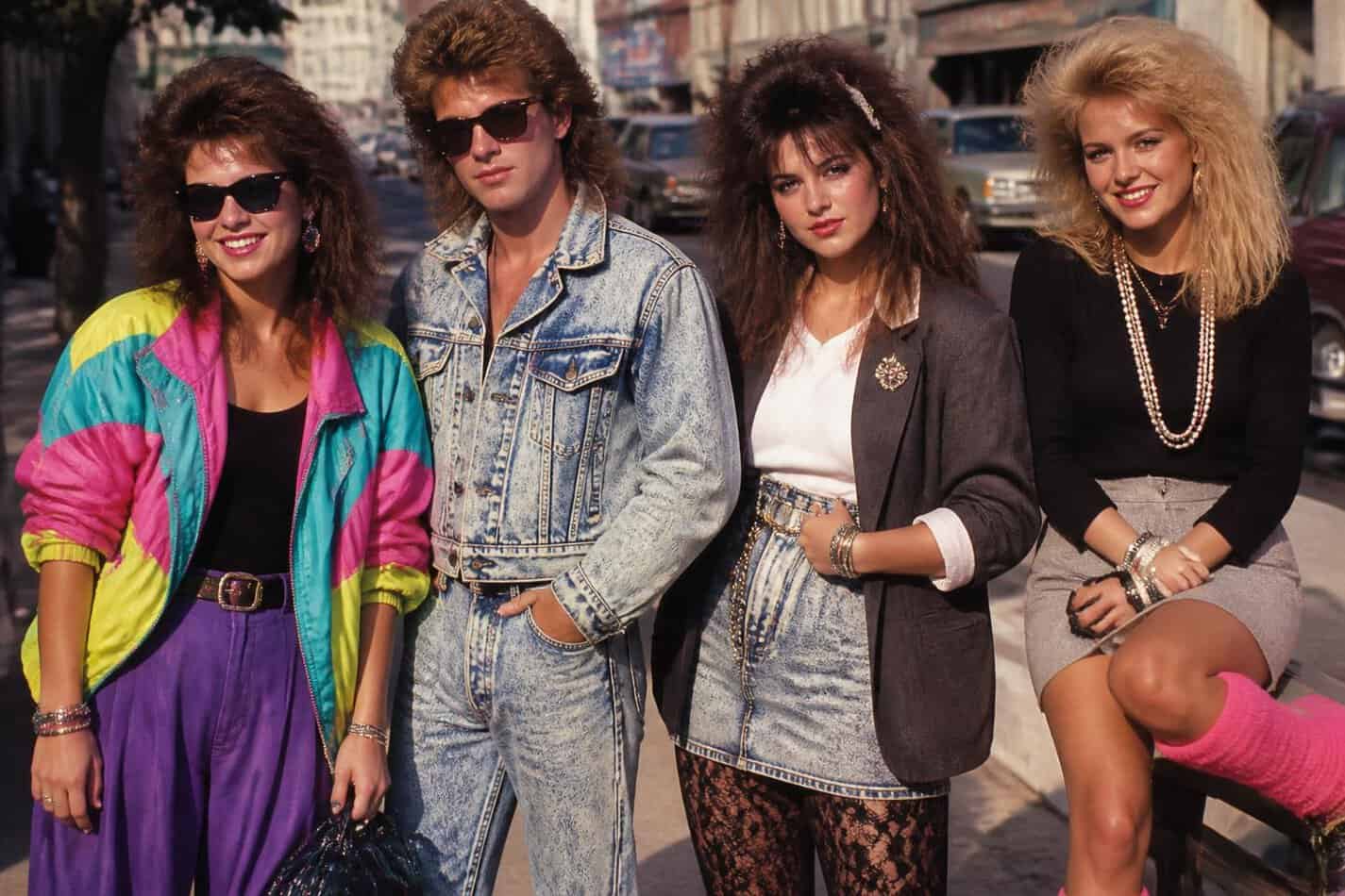 Four friends posing on a city street in neon windbreakers, acid wash denim and big 80s hair